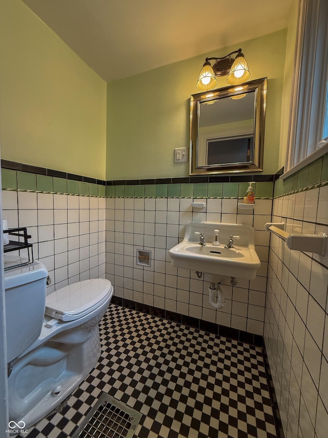 half bathroom with toilet, tile walls, wainscoting, a sink, and tile patterned floors