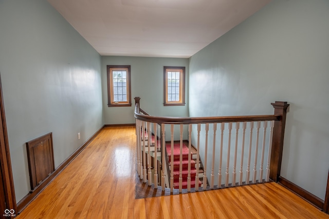 hall featuring wood finished floors, baseboards, and an upstairs landing