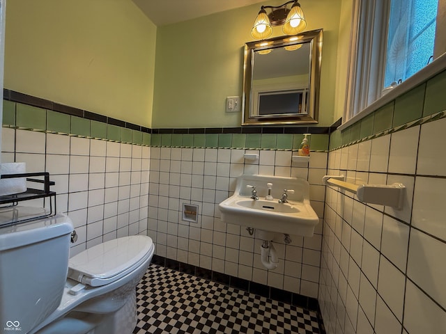 half bathroom featuring toilet, tile walls, a wainscoted wall, tile patterned floors, and a sink