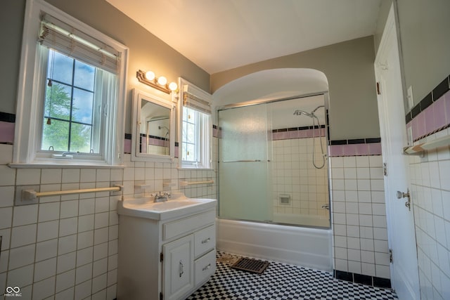 bathroom featuring tile walls, vanity, combined bath / shower with glass door, a wainscoted wall, and tile patterned floors
