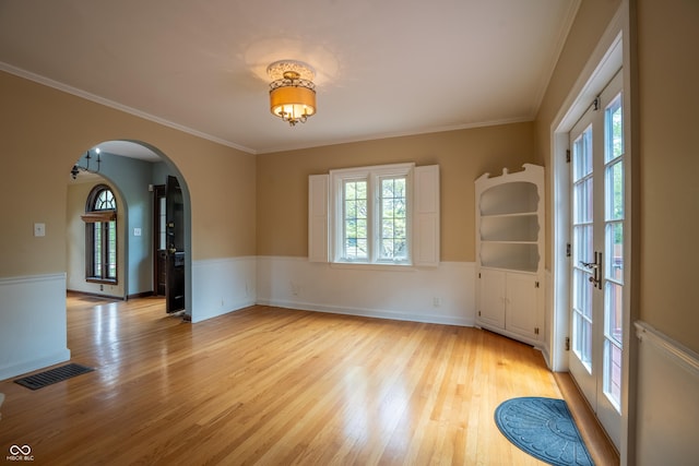 empty room with arched walkways, light wood-style floors, ornamental molding, and a wainscoted wall