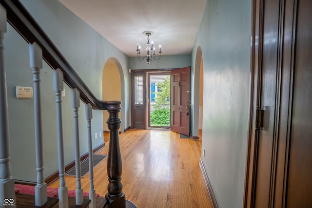 foyer with arched walkways, light wood-style floors, a chandelier, baseboards, and stairs
