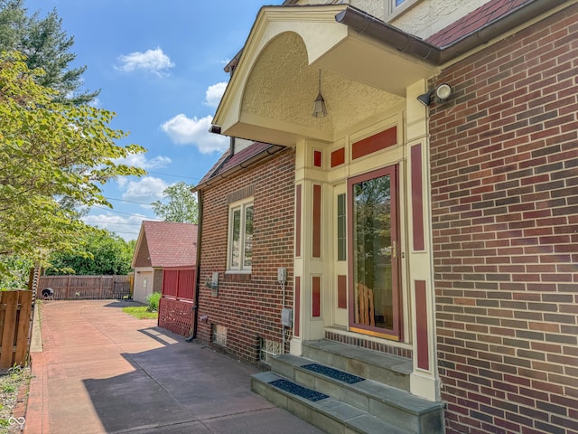view of exterior entry with fence, brick siding, and a detached garage