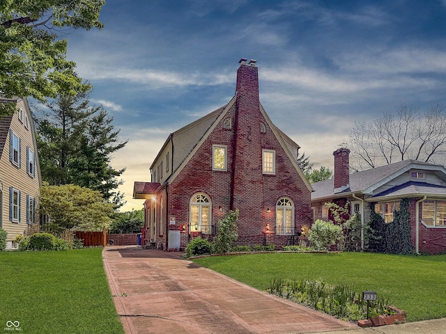 tudor home featuring brick siding, driveway, and a chimney