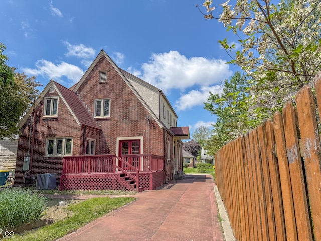 view of side of property with cooling unit, brick siding, a deck, and fence