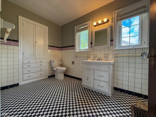 bathroom featuring tile walls, toilet, wainscoting, vanity, and tile patterned floors