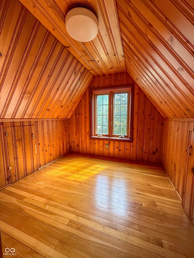 additional living space featuring light wood finished floors, wood walls, and vaulted ceiling