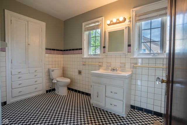 bathroom with tile walls, a wainscoted wall, toilet, vanity, and tile patterned floors