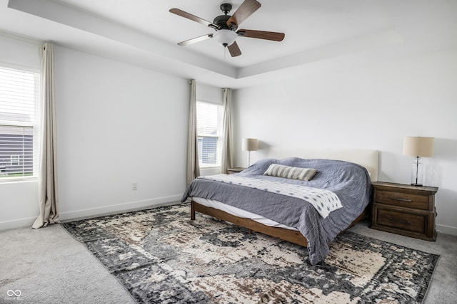 carpeted bedroom with a tray ceiling, ceiling fan, and baseboards