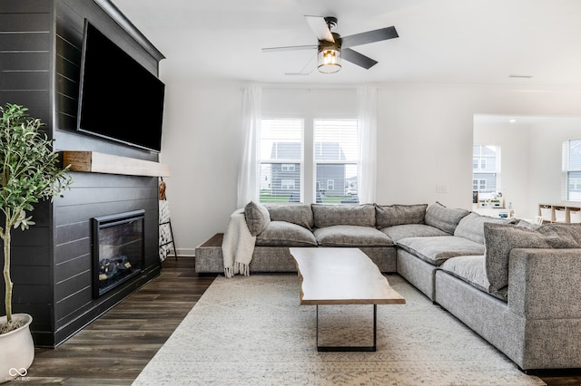 living area featuring a ceiling fan, a wealth of natural light, a glass covered fireplace, and dark wood-style floors