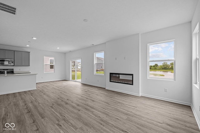 6219 Medina Spirit Dr, Indianapolis, IN 46237 - unfurnished living room with light wood-style flooring, a glass covered fireplace, and recessed lighting