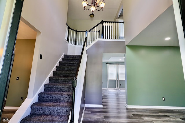 stairway with wood finished floors, a towering ceiling, baseboards, and a chandelier