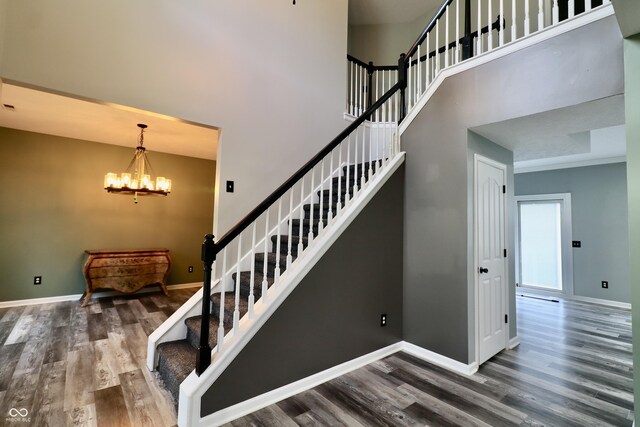 staircase featuring wood finished floors, a towering ceiling, a chandelier, and baseboards