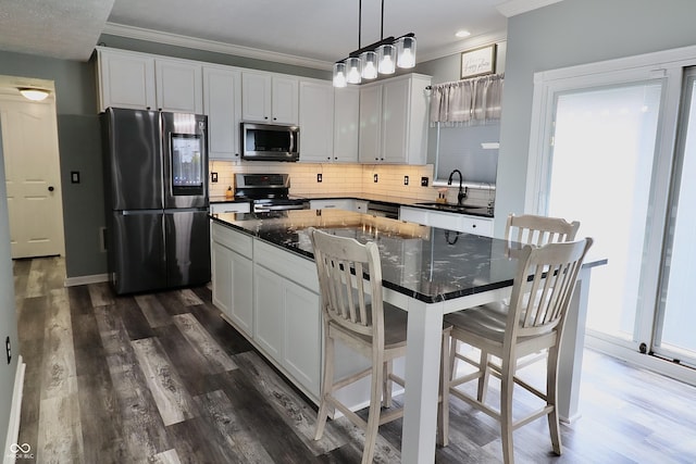 kitchen with appliances with stainless steel finishes, a sink, crown molding, decorative backsplash, and white cabinetry
