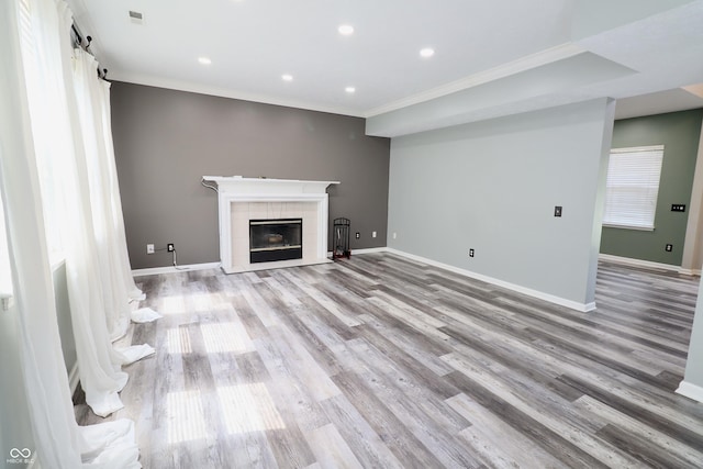 unfurnished living room with crown molding, light wood finished floors, recessed lighting, baseboards, and a tiled fireplace