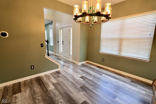 unfurnished dining area with a chandelier, baseboards, wood finished floors, and healthy amount of natural light