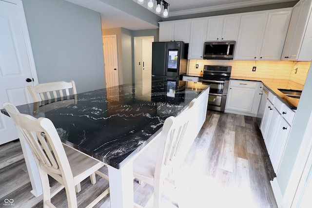 kitchen with appliances with stainless steel finishes, dark wood-style flooring, tasteful backsplash, white cabinetry, and a large island