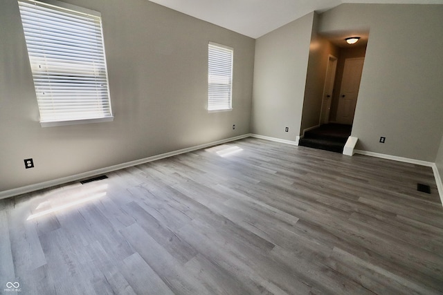 empty room featuring vaulted ceiling, wood finished floors, and baseboards