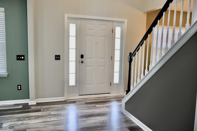 entryway with wood finished floors, healthy amount of natural light, stairway, and baseboards