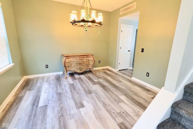 unfurnished dining area with light wood finished floors, a chandelier, baseboards, and stairway