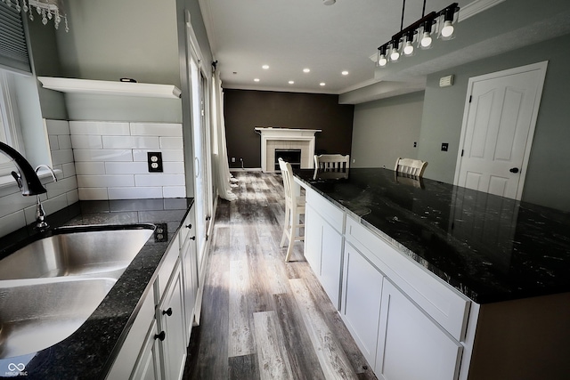 kitchen with a sink, wood finished floors, white cabinetry, recessed lighting, and a tile fireplace