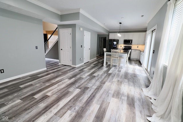 unfurnished living room featuring wood finished floors, baseboards, crown molding, and stairway