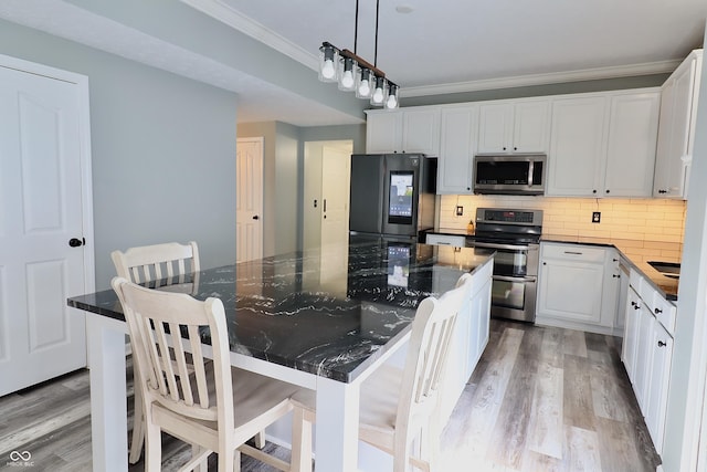 kitchen featuring stainless steel appliances, ornamental molding, light wood-style floors, decorative backsplash, and white cabinets