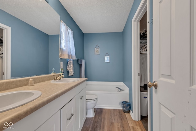 full bath featuring wood finished floors, toilet, a garden tub, a walk in closet, and a textured ceiling