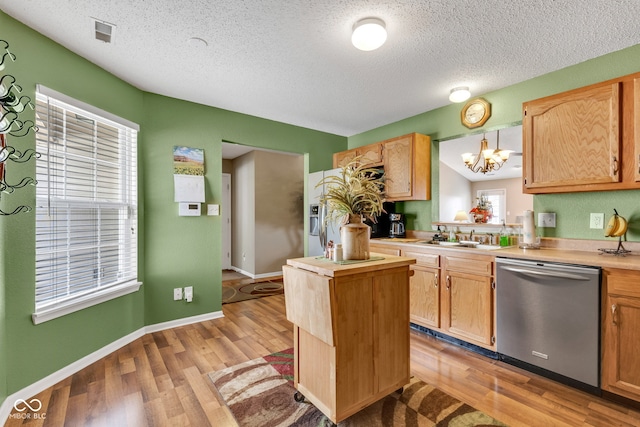 kitchen featuring stainless steel dishwasher, a sink, a textured ceiling, light countertops, and light wood-style floors