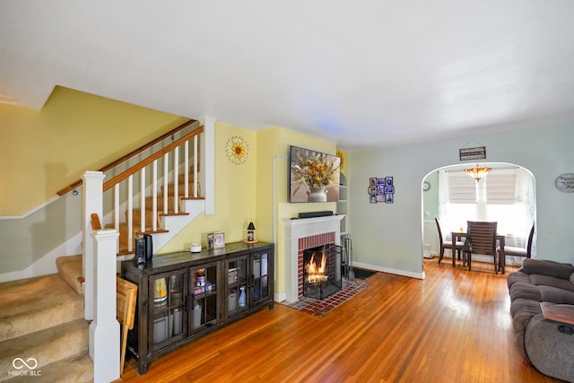 living area featuring baseboards, stairs, wood finished floors, arched walkways, and a fireplace