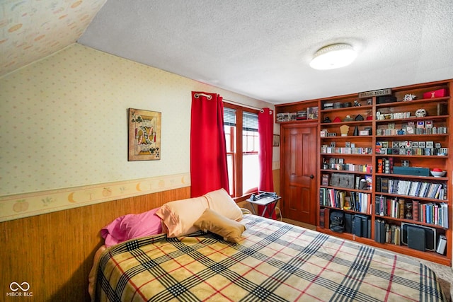 bedroom featuring a wainscoted wall, a textured ceiling, and wooden walls