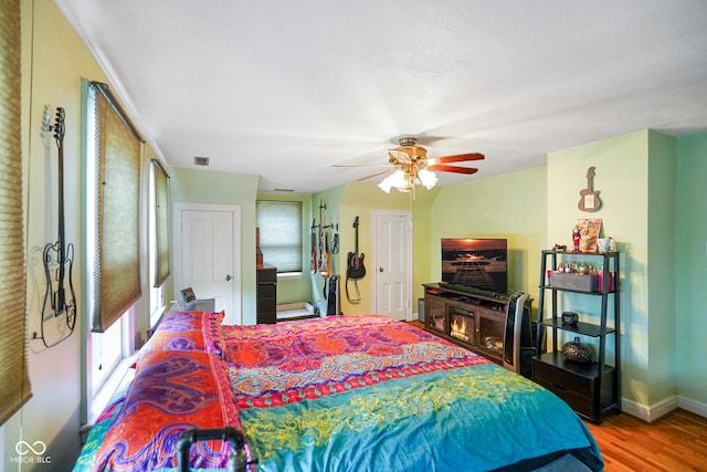 bedroom with wood finished floors, two closets, visible vents, baseboards, and ceiling fan