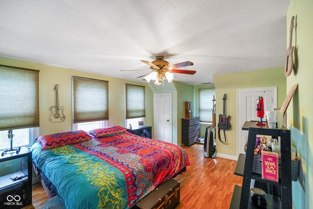 bedroom featuring a textured ceiling, light wood-style flooring, baseboards, and ceiling fan