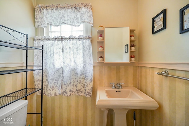 bathroom with a sink, toilet, and wallpapered walls