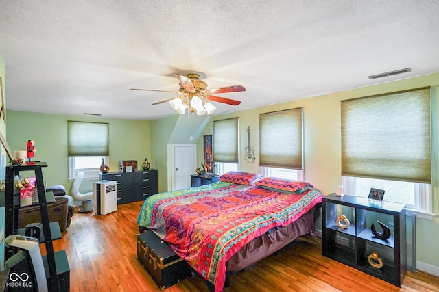 bedroom featuring multiple windows, visible vents, a textured ceiling, and wood finished floors