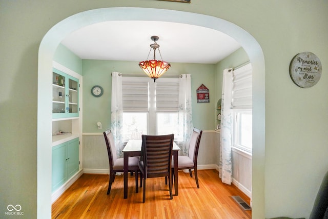 dining area with arched walkways, light wood-style floors, visible vents, and baseboards