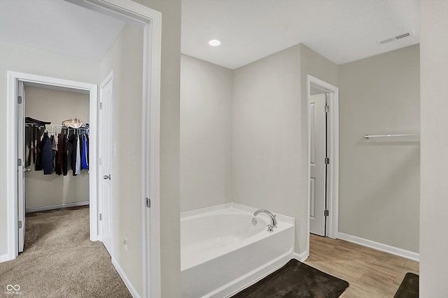 full bathroom with a garden tub, visible vents, baseboards, and a spacious closet