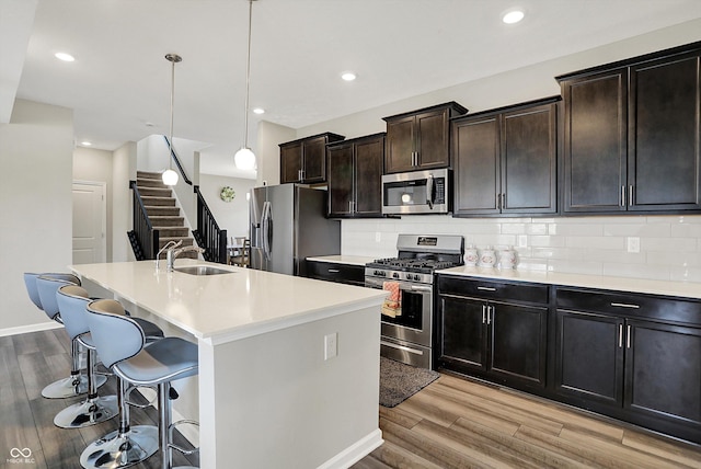 kitchen featuring a sink, light wood-style flooring, a kitchen island with sink, and appliances with stainless steel finishes