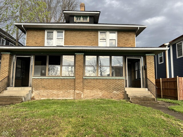rear view of property featuring brick siding, fence, and a lawn
