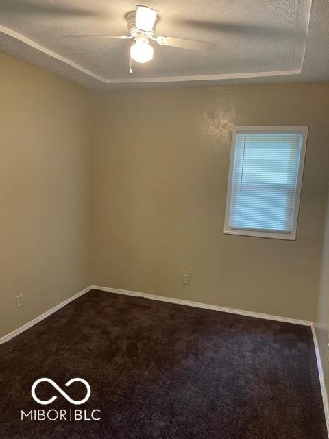 spare room with a textured ceiling, dark colored carpet, a ceiling fan, a tray ceiling, and baseboards