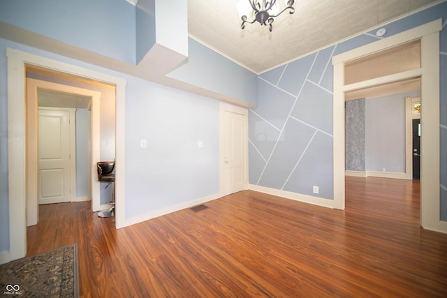 spare room featuring baseboards, ornamental molding, visible vents, a chandelier, and wood finished floors