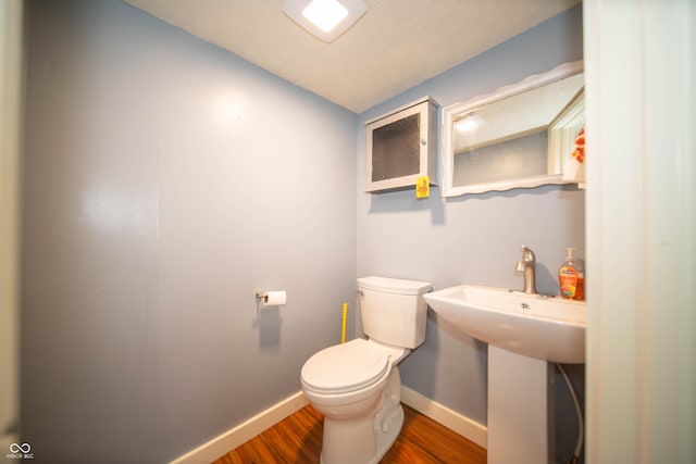 half bathroom featuring toilet, baseboards, a sink, and wood finished floors