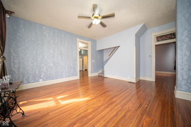 unfurnished living room with ceiling fan, baseboards, wallpapered walls, and wood finished floors