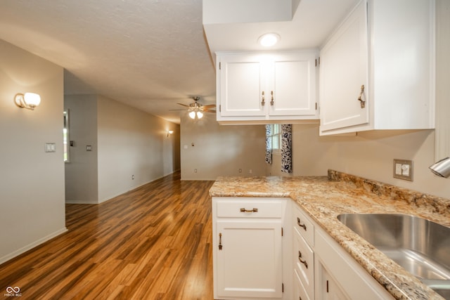 kitchen with light wood-style flooring, a ceiling fan, a sink, white cabinetry, and light stone countertops