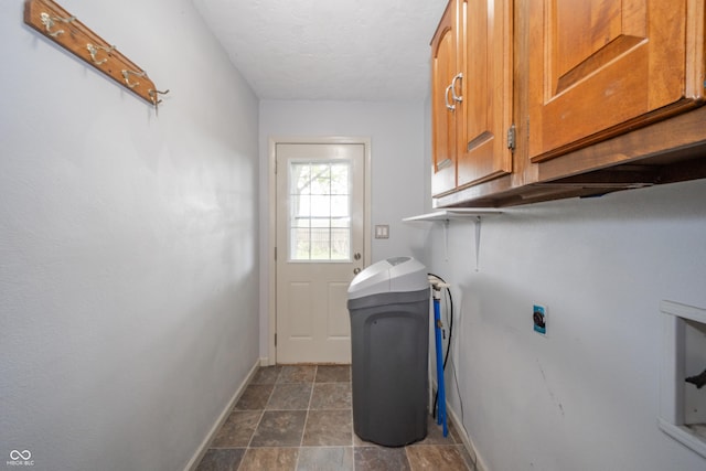washroom with electric dryer hookup, cabinet space, baseboards, and stone finish floor