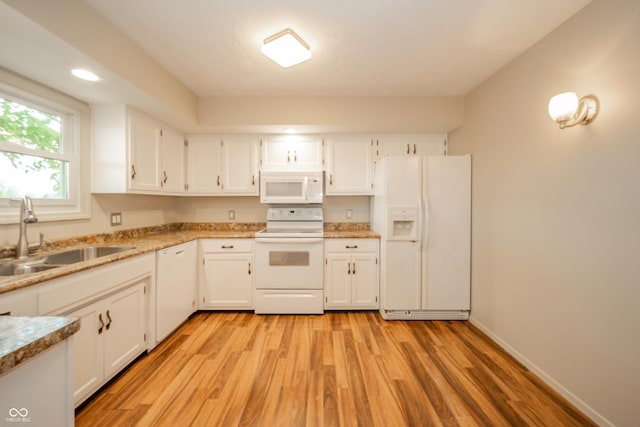 kitchen with light wood finished floors, white cabinets, a sink, and white appliances