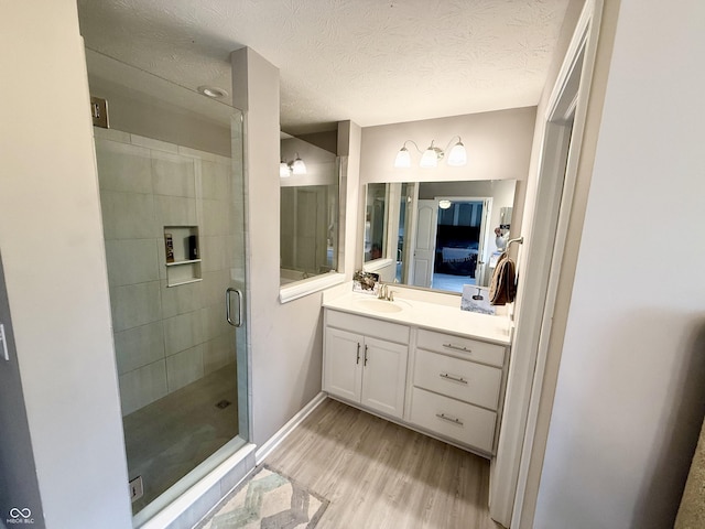 full bathroom with wood finished floors, vanity, a textured ceiling, a shower stall, and baseboards