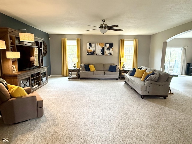 living area with carpet flooring, arched walkways, a ceiling fan, and plenty of natural light