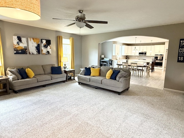 living room with light colored carpet, baseboards, a ceiling fan, and arched walkways