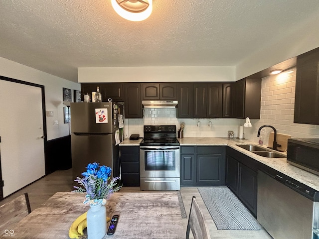 kitchen featuring under cabinet range hood, a sink, light countertops, tasteful backsplash, and appliances with stainless steel finishes